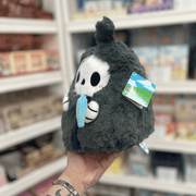 Mini Squishable Reaper plush toy held in hand in a gift shop, side view holding scythe