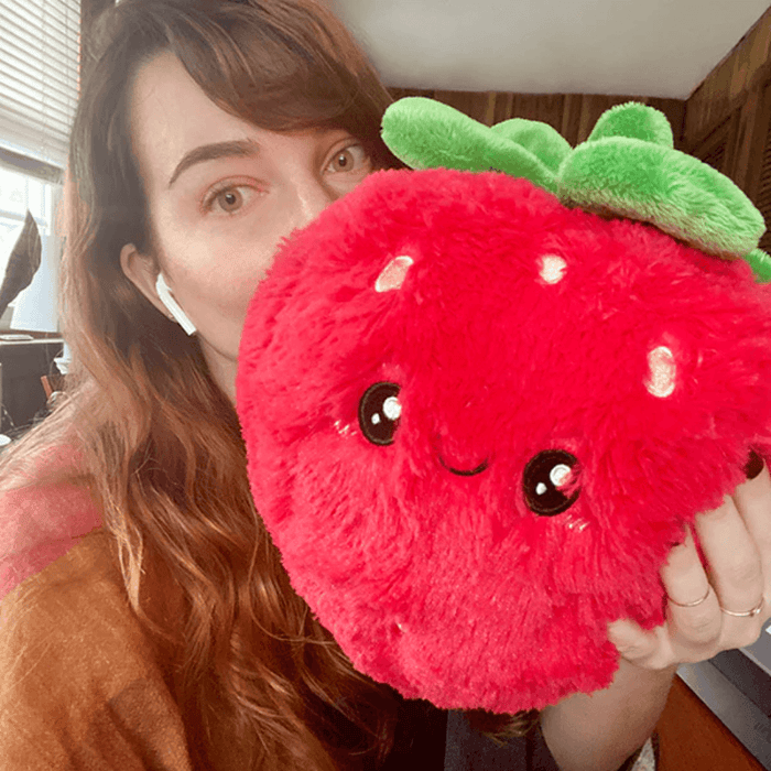 Person holding Squishable Mini Comfort Food Strawberry plush toy in a cosy lifestyle photo