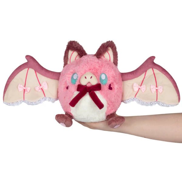 Front view of pink Squishable Mini Sweetheart Bat plush with wings spread, lace trim and velvet bow, held in hand