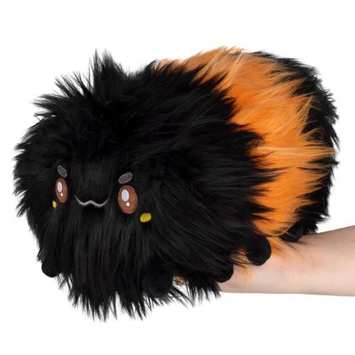 Front view of Squishable Mini Woolly Caterpillar plush with long black-and-orange fur, held in hand
