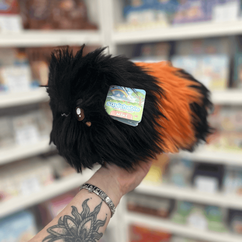Mini Squishable Woolly Caterpillar plush held in hand in a gift shop, side view