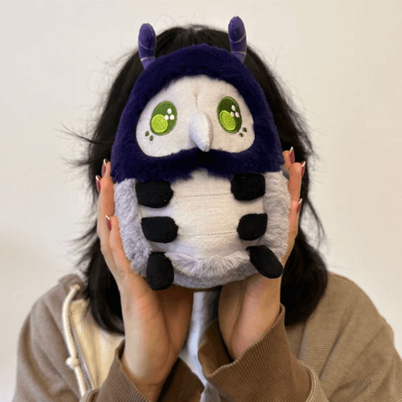 Person holding Squishable Plague Doctor Bug plush with purple hood and green eyes