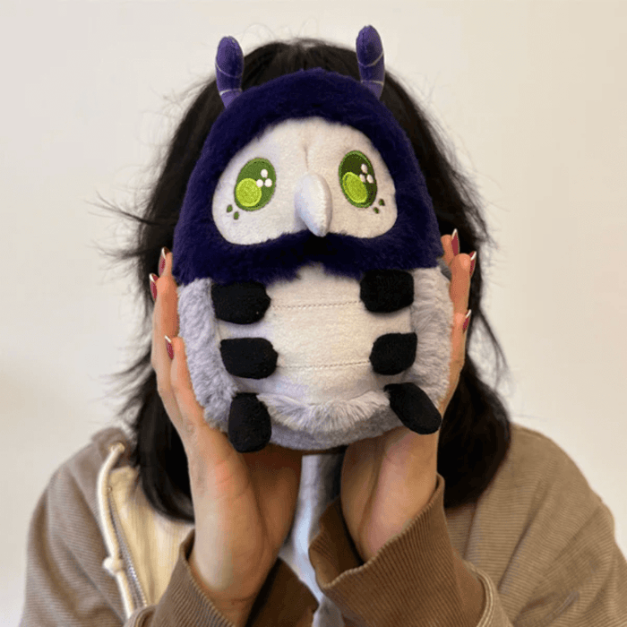 Person holding Squishable Plague Doctor Bug plush with purple hood and green eyes