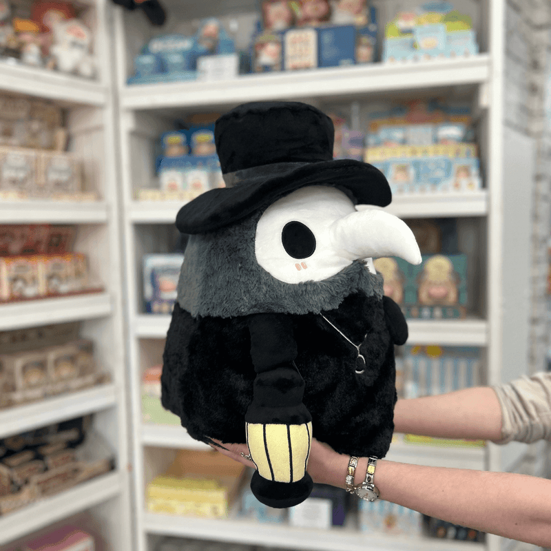 Squishable Plague Doctor plush toy held in hands in a gift shop, angled side view