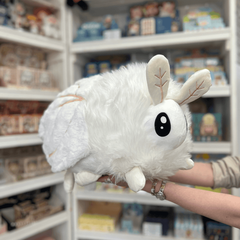 Squishable Poodle Moth plush toy held in hands in a gift shop, angled side view