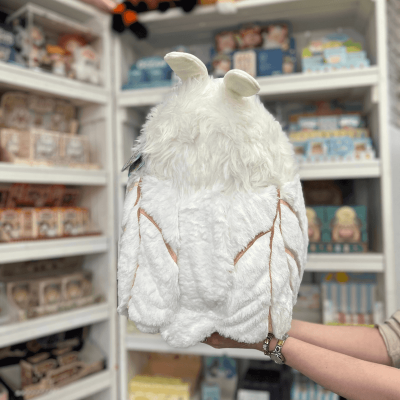 Squishable Poodle Moth plush toy held in hands in a gift shop, back view showing wings