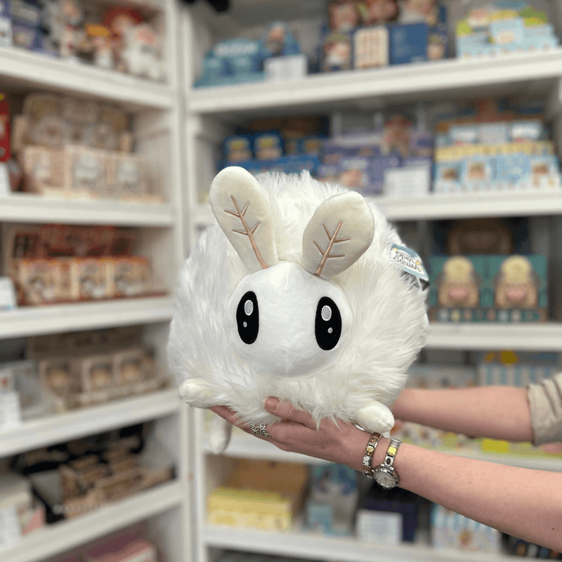 Squishable Poodle Moth plush toy held in hands in a gift shop, front view