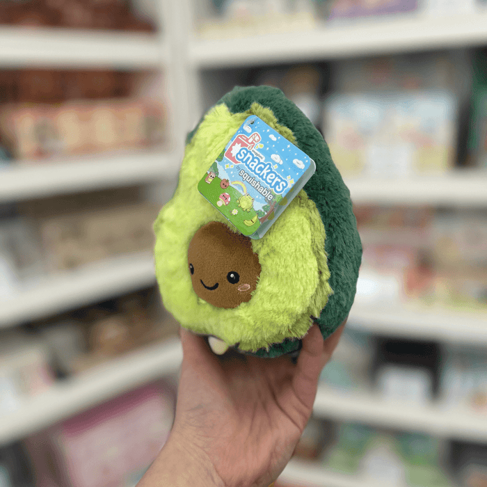 Squishable Snacker Avocado plush toy held in hand with tag visible