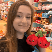 Squishable Snacker Cherries plush toy being held in a shop for size comparison