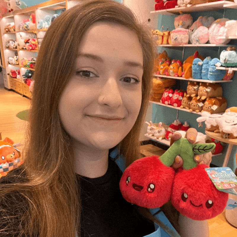 Squishable Snacker Cherries plush toy being held in a shop for size comparison