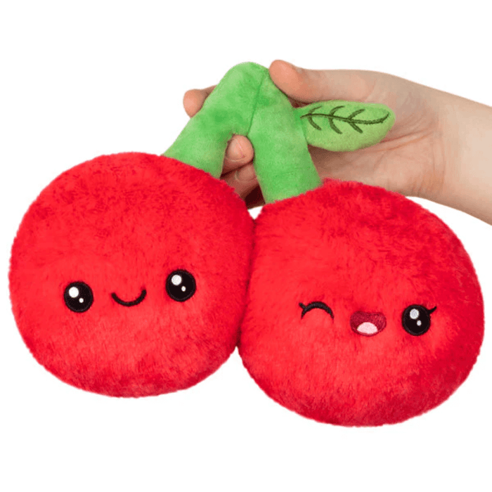 Hand holding Squishable Snacker Cherries plush toy with two red cherries and smiling faces