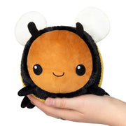 Front view of the Squishable Snacker Fuzzy Bumblebee plushie being held in two hands, with a cute smiling face and big white wings.