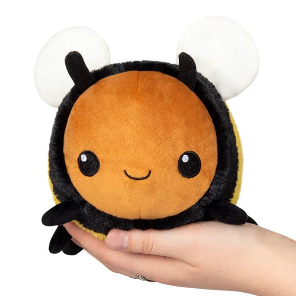 Front view of the Squishable Snacker Fuzzy Bumblebee plushie being held in two hands, with a cute smiling face and big white wings.