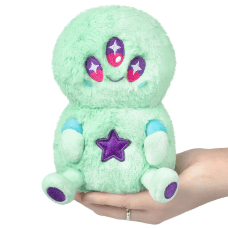 Front view of the Squishable Snacker Green Alien plush toy with three eyes and purple star detail