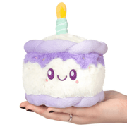 Front view of the Squishable Snacker Happy Birthday Cake plush toy with lilac frosting and candle detail