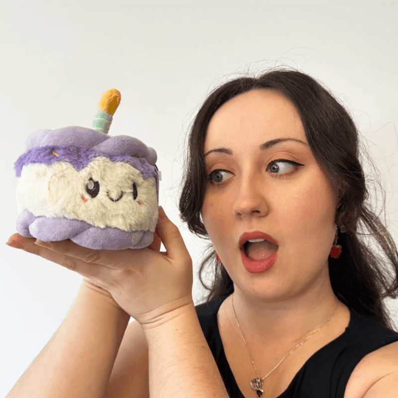 Woman holding the Squishable Snacker Happy Birthday Cake plush toy for size comparison