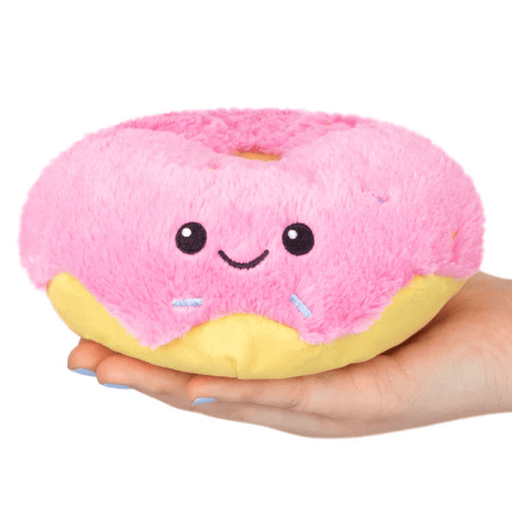 Hand holding Squishable Snacker Pink Donut plush toy with smiling face and sprinkle details