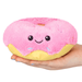 Hand holding Squishable Snacker Pink Donut plush toy with smiling face and sprinkle details