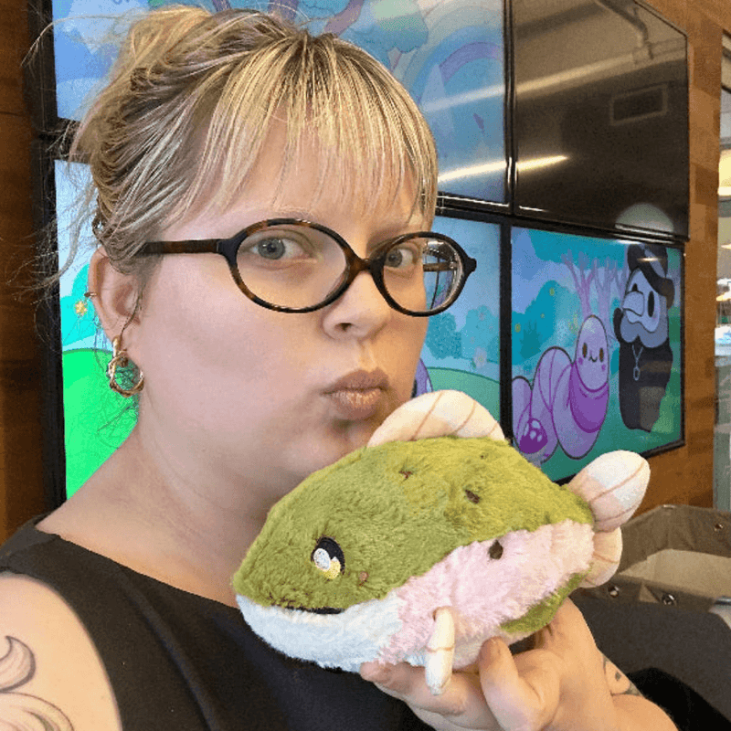 Woman holding the Squishable Snacker Rainbow Trout plush toy for size comparison