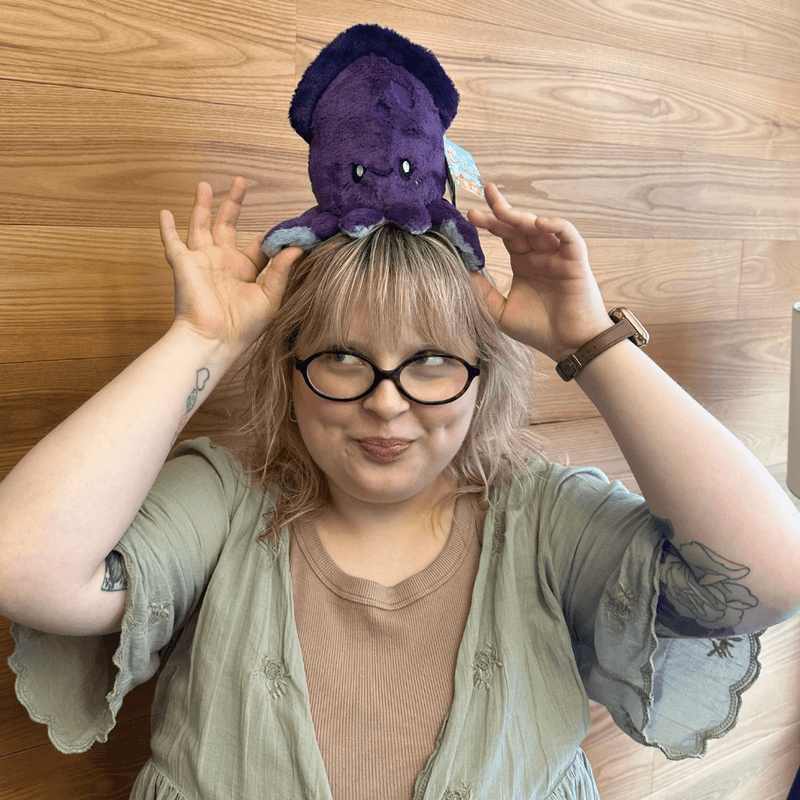 Squishable Snacker Squid plush balanced playfully on a person's head