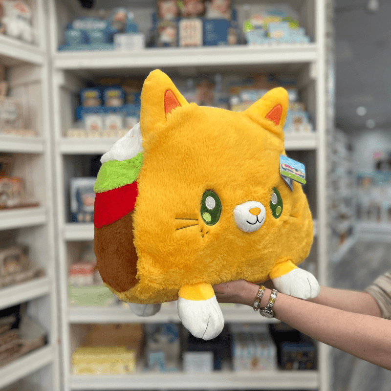 Squishable Taco Cat plush toy held in hands in a gift shop, angled side view