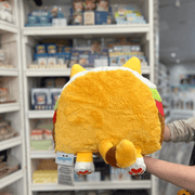 Squishable Taco Cat plush toy held in hands in a gift shop, back view showing tail and taco filling detail