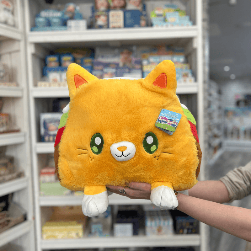 Squishable Taco Cat plush toy held in hands in a gift shop, front view