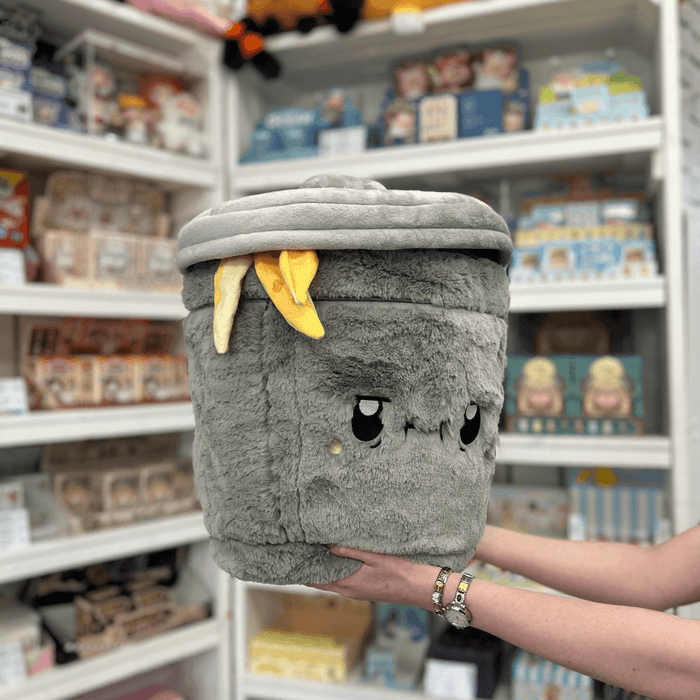 Squishable Trash Can plush toy held in hands in a gift shop, angled front view with banana peel detail