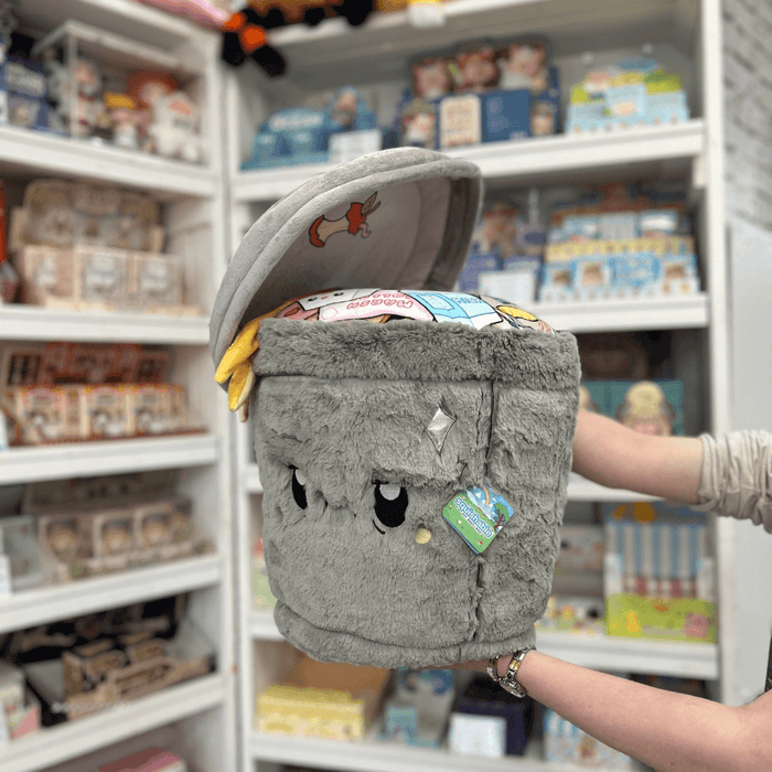 Squishable Trash Can plush toy held in hands in a gift shop, angled front view with lid open