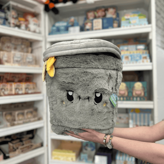 Squishable Trash Can plush toy held in hands in a gift shop, front view