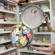 Squishable Trash Can plush toy held in hands in a gift shop, opened to show illustrated rubbish inside