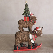 Festive stacked Highland cows on skis displayed on a table


