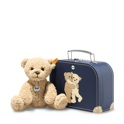 Steiff Ben Teddy Bear in beige plush sitting beside a blue suitcase with teddy bear design on a white background