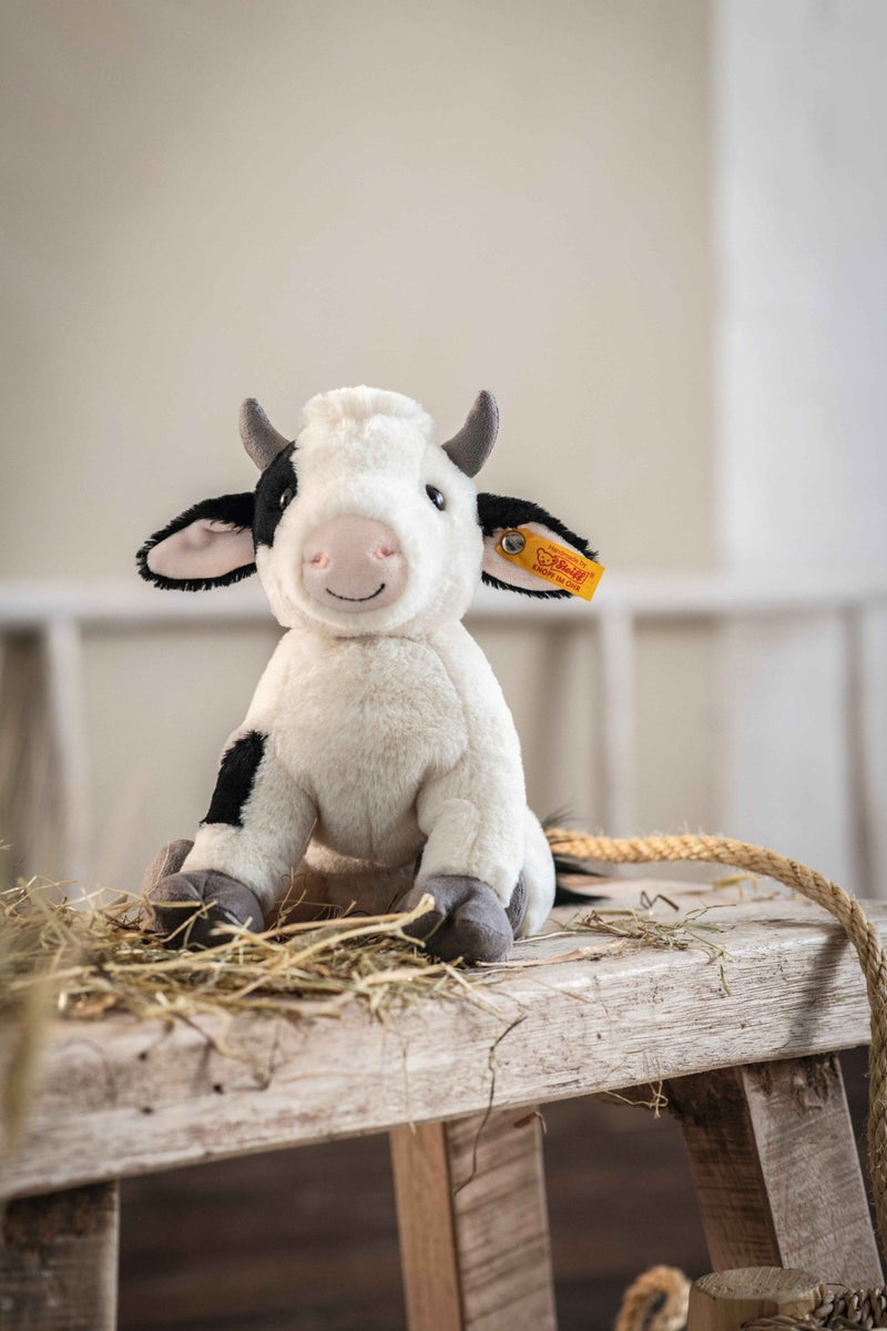 Lifestyle shot of Steiff Cobb Cow plush on rustic bench with straw – Steiff bears gift idea