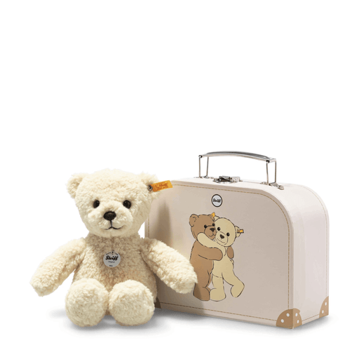 Steiff Mila Teddy Bear in vanilla-yellow teddy fleece sitting beside a cream suitcase with Mila and Ben design on a white background