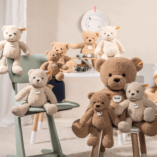 Steiff Mila Teddy Bear in suitcase shown in a nursery scene with other teddy bears and soft neutral décor