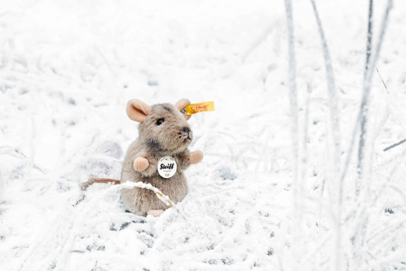 Steiff Piff Mouse plush photographed outdoors in snowy grass with yellow ear tag.