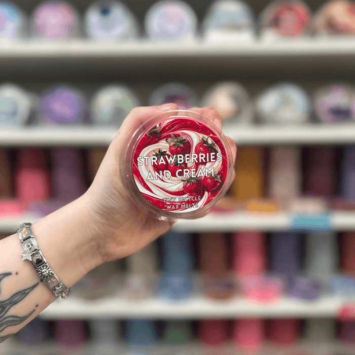 Strawberries and Cream wax melt pot held in hand with colourful wax melt display in the background