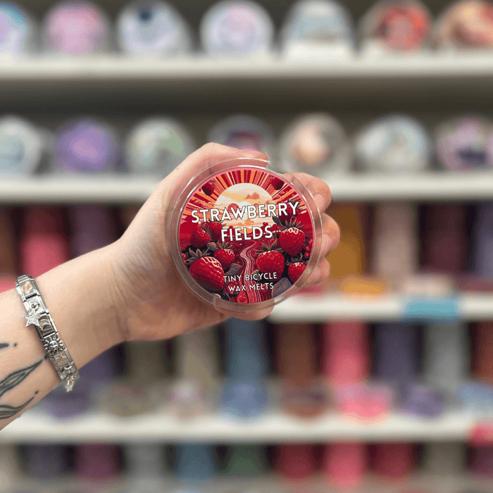 Strawberry Fields wax melt pot held in hand with colourful wax melt display in the background