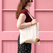 Side view of a woman carrying a cute capybara canvas tote bag against a pink wall, showing the fluffy animal decoration.