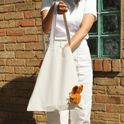SUCK UK Peeky Bunny canvas tote bag held by its long shoulder straps with a plush brown rabbit on the front.