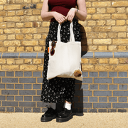 Full-length view of a woman holding a cream SUCK UK capybara tote bag with the plush animal head visible on the lower front.