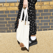 Woman holding a natural cotton SUCK UK Peeky Capybara tote bag with a fluffy brown capybara head peeking out near the bottom.
