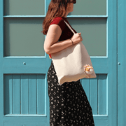 Woman wearing a cream canvas Peeky Cat tote bag over her shoulder beside a turquoise doorway.