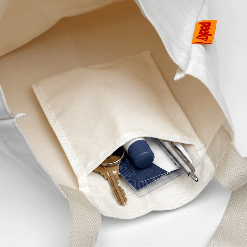 Interior of the natural cotton Peeky tote bag showing its stitched pocket holding keys, a pen and other small essentials.
