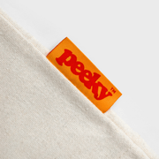 Close-up of the bright orange Peeky woven fabric label stitched into the cream cotton canvas shopper.