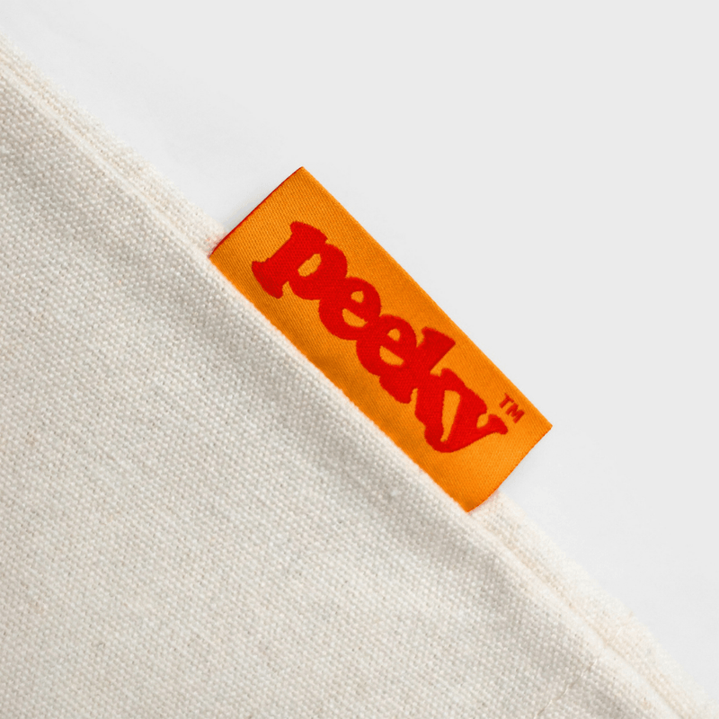 Close-up of the bright orange Peeky woven fabric label stitched into the cream cotton canvas shopper.