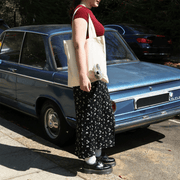 Woman carrying the cream Peeky Donkey tote bag with a plush animal decoration while standing beside a vintage blue car.