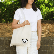 Woman carrying a natural cotton SUCK UK Peeky Panda tote bag with a fluffy black-and-white panda head peeking from the lower corner.