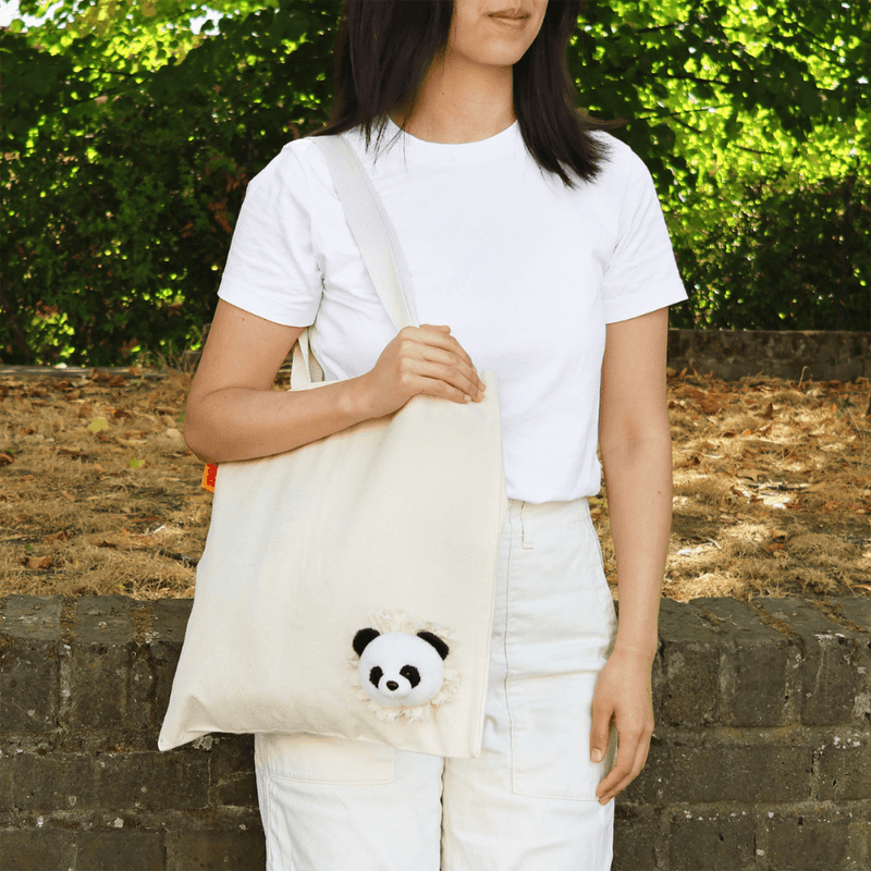 Woman carrying a natural cotton SUCK UK Peeky Panda tote bag with a fluffy black-and-white panda head peeking from the lower corner.